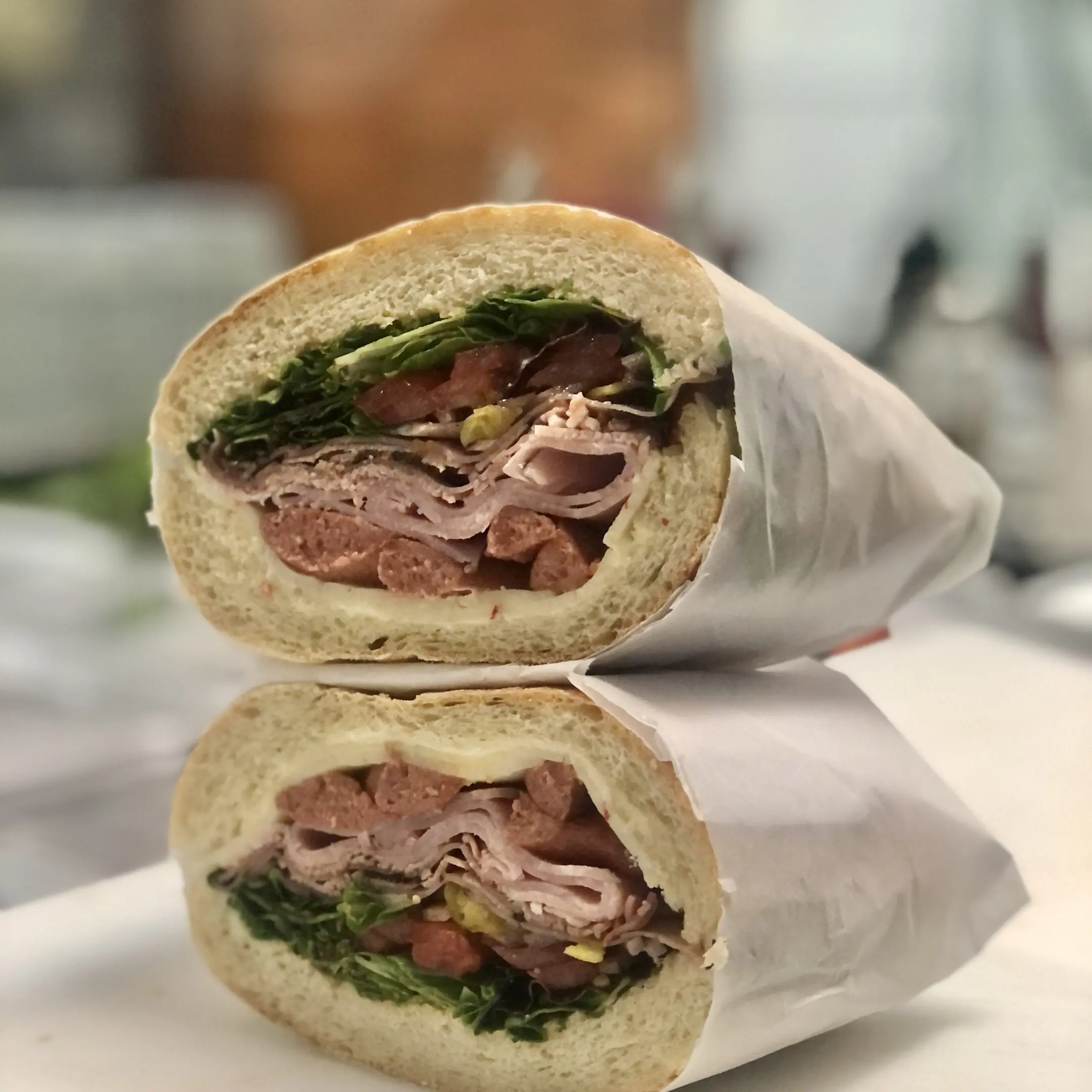 67b7423e2bc7b_F0054E58-2583-4E0E-AF58-306559FFA704 A sandwich cut in half on top of a table.